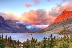 the sun is setting over a mountain lake with trees around it and mountains in the background