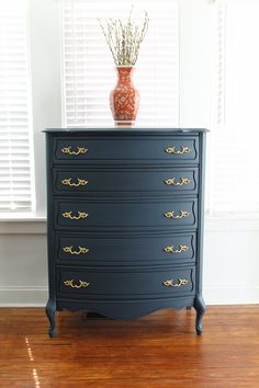 a black dresser with gold handles and drawers in front of a white window covered by shutters