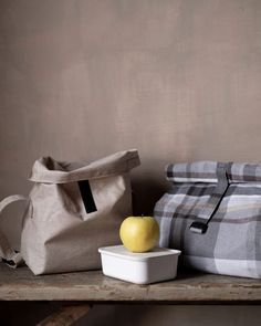 an apple sitting on top of a wooden table next to a bag and container with a lid