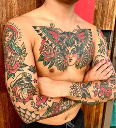 a man with tattoos standing in front of a wooden wall and wearing his arms crossed