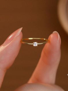 a woman's hand holding a gold ring with a single diamond on the side