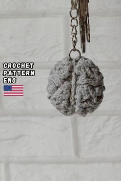 a crochet brain keychain hanging from a hook on a brick wall