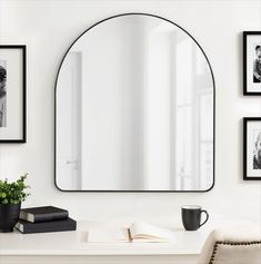 a white desk with a mirror, book and coffee cup on it in front of some framed photos