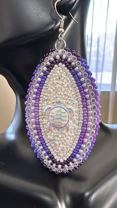 a pair of purple and white beaded earrings sitting on top of a mannequin