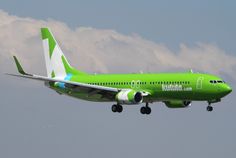 a green and white plane is flying in the sky with clouds behind it on a cloudy day