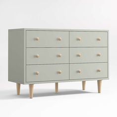 a white dresser with wooden legs and knobs on the bottom drawer, in front of a plain background