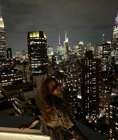 a woman standing on top of a building looking at the city lights in the distance