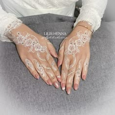 a woman's hands with white lace on them sitting on a gray chair and holding onto her arm