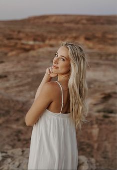 a woman standing in the desert with her hand on her chin and looking off into the distance