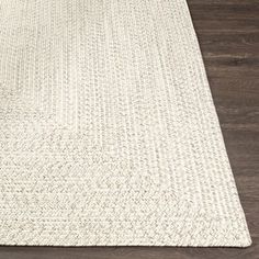 a white rug on top of a wooden floor next to a vase with flowers in it