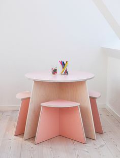 two stools and a table with pencils on it in front of a white wall