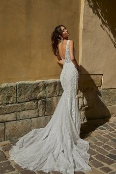 a woman in a white wedding dress leaning against a wall with her back to the camera