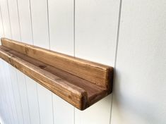 a wooden shelf mounted to the side of a white wall with wood planks on it