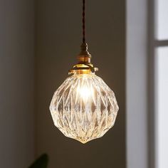 a clear glass light hanging from a cord in front of a white wall and window