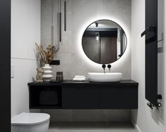 a white toilet sitting next to a bathroom sink under a round mirror on a wall