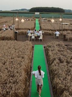 a woman walking down a green path in the middle of a field