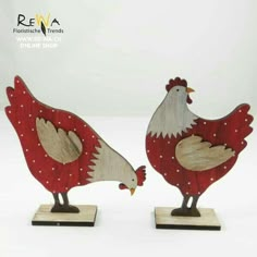 two wooden rooster figurines standing next to each other on top of a white surface