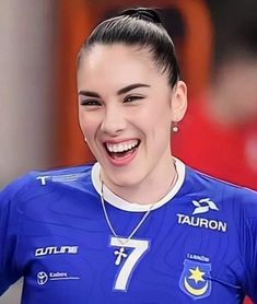 a smiling woman wearing a blue shirt and silver necklace with the number seven on it