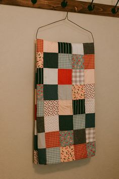 a patchwork quilt hanging on a wall with clothes pins attached to the pegs