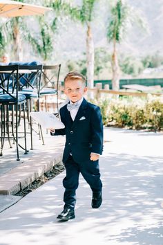 a young boy in a suit and bow tie walking down the street with an umbrella