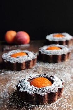 small pastries are covered with powdered sugar on a wooden table next to fruit