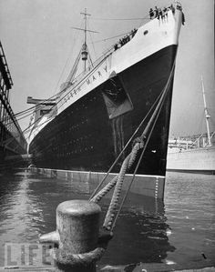 an old photo of a large ship docked in the water next to another boat with people on it