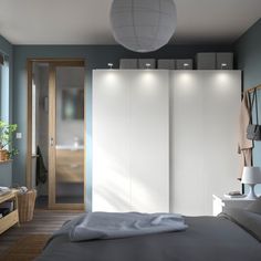 a bedroom with blue walls and white closets next to a bed in front of a window