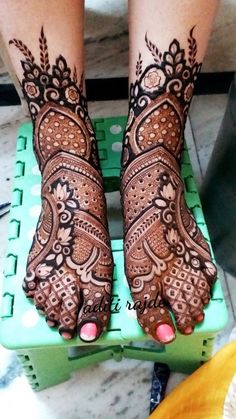 the legs and feet of a woman with henna tattoos on their hands, sitting on top of a green crate