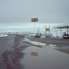 an empty gas station with puddles of water on the ground and signs in front