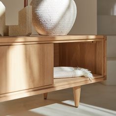 a white vase sitting on top of a wooden table next to a shelf with towels