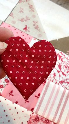 someone is holding up a heart shaped piece of fabric in front of a patchwork quilt