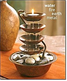 a water fountain with rocks in it and a lit candle on the top that reads, water fire earth metal