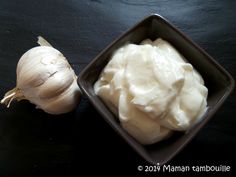 a bowl of mayonnaise next to a garlic on a black surface with a white bulb