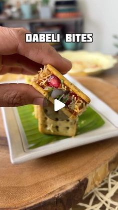 a person is holding a small sandwich on a plate with the caption dabeli bites