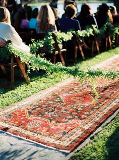 people are sitting in chairs on the grass near an area rug that has plants growing out of it