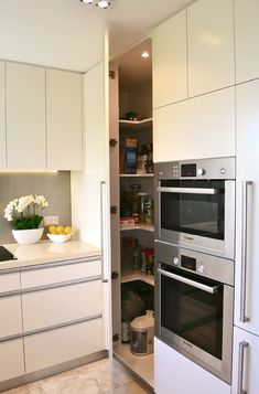 a kitchen with white cabinets and stainless steel ovens in the center, along with an open pantry