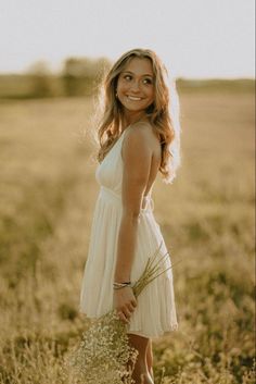 a woman in a white dress is standing in a field with tall grass and looking at the camera