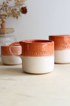 three orange and white mugs sitting on top of a table