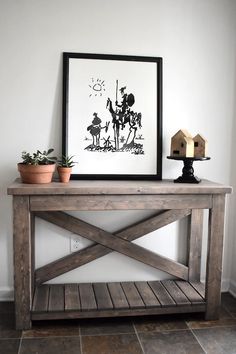 a wooden table with two potted plants on it and a framed picture above it