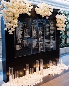 an arrangement of flowers and candles on display in front of a wall with seating cards