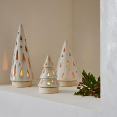 three white candles are sitting on a shelf next to some pine cones with lights in them