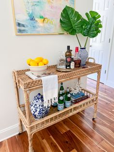 a wicker bar cart with drinks on it in a living room next to a painting