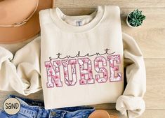 a white shirt with the word nurse written in pink on it next to some shoes and a hat