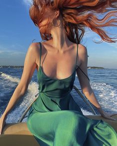 a woman with long red hair riding on a boat in the ocean while wearing a green dress