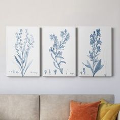 three blue and white paintings on the wall above a couch in a living room with orange pillows