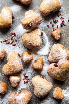 several heart shaped pastries are on a table with powdered sugar and rose petals