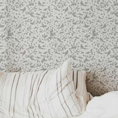 a bed with a white pillow on top of it next to a wallpapered headboard