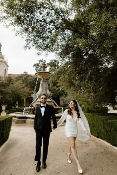 a bride and groom walking in front of a fountain