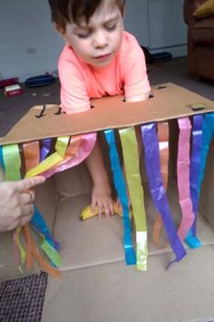 a young child sitting in a cardboard box with streamers on the floor next to it