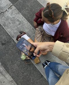 a woman sitting on top of a skateboard holding a smart phone in her hand